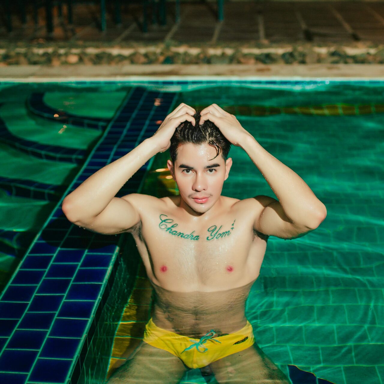 A young man with tattoos enjoys a refreshing swim in a clear blue pool.