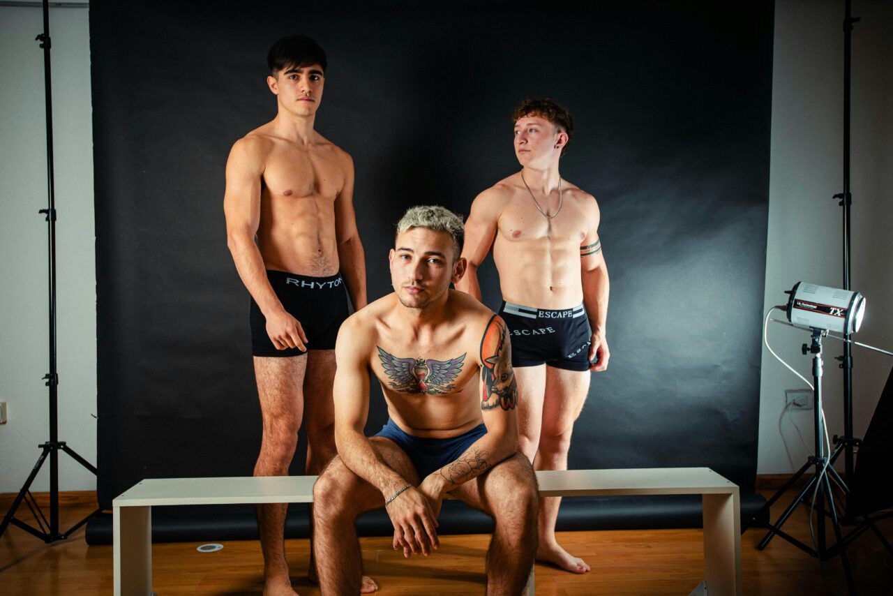 A striking studio photoshoot featuring topless male models with tattoos and various poses.