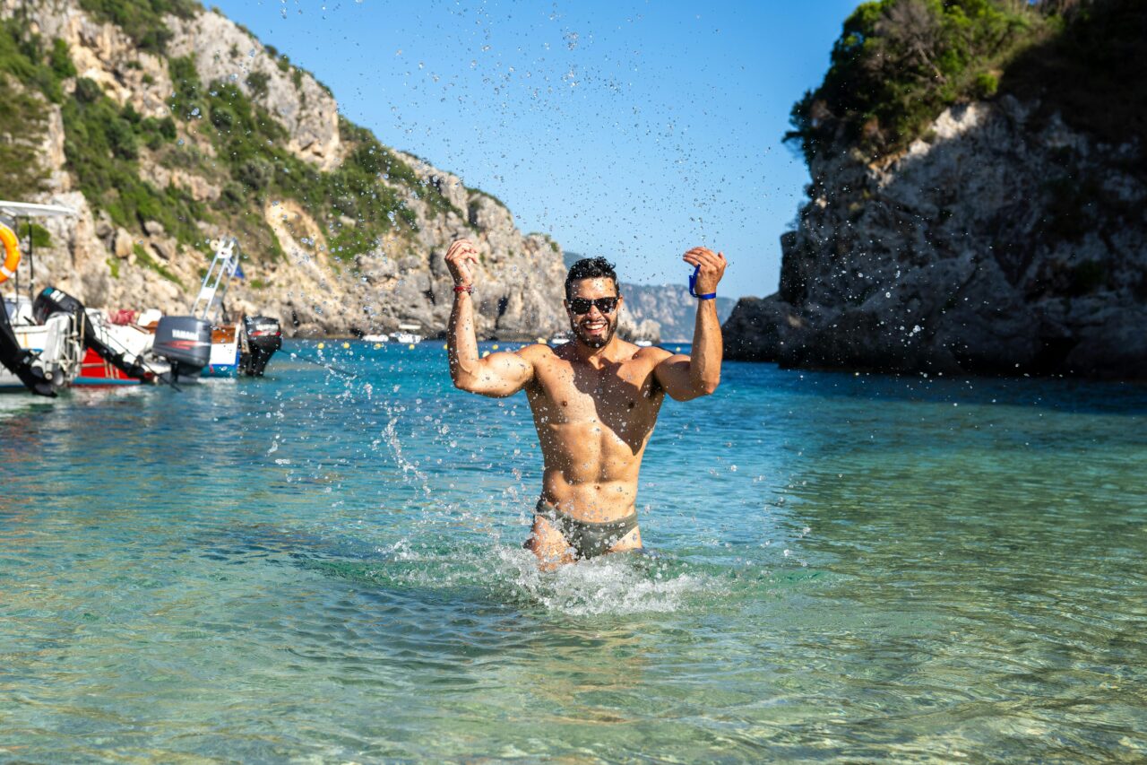 Young man splashing water and having fun on a sunny day at a beautiful beach in Corfu, Greece.