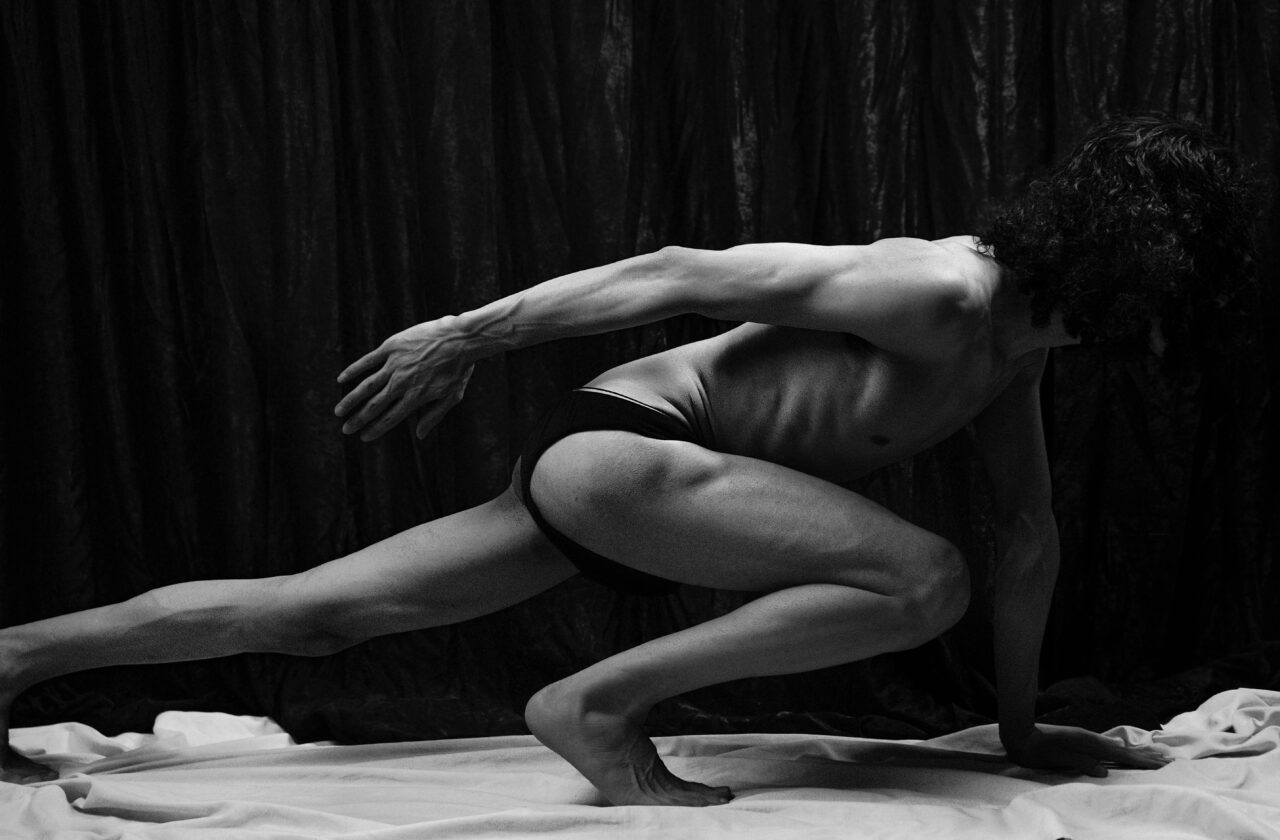 A monochrome image of a topless man in a dynamic stretch pose, showcasing musculature.