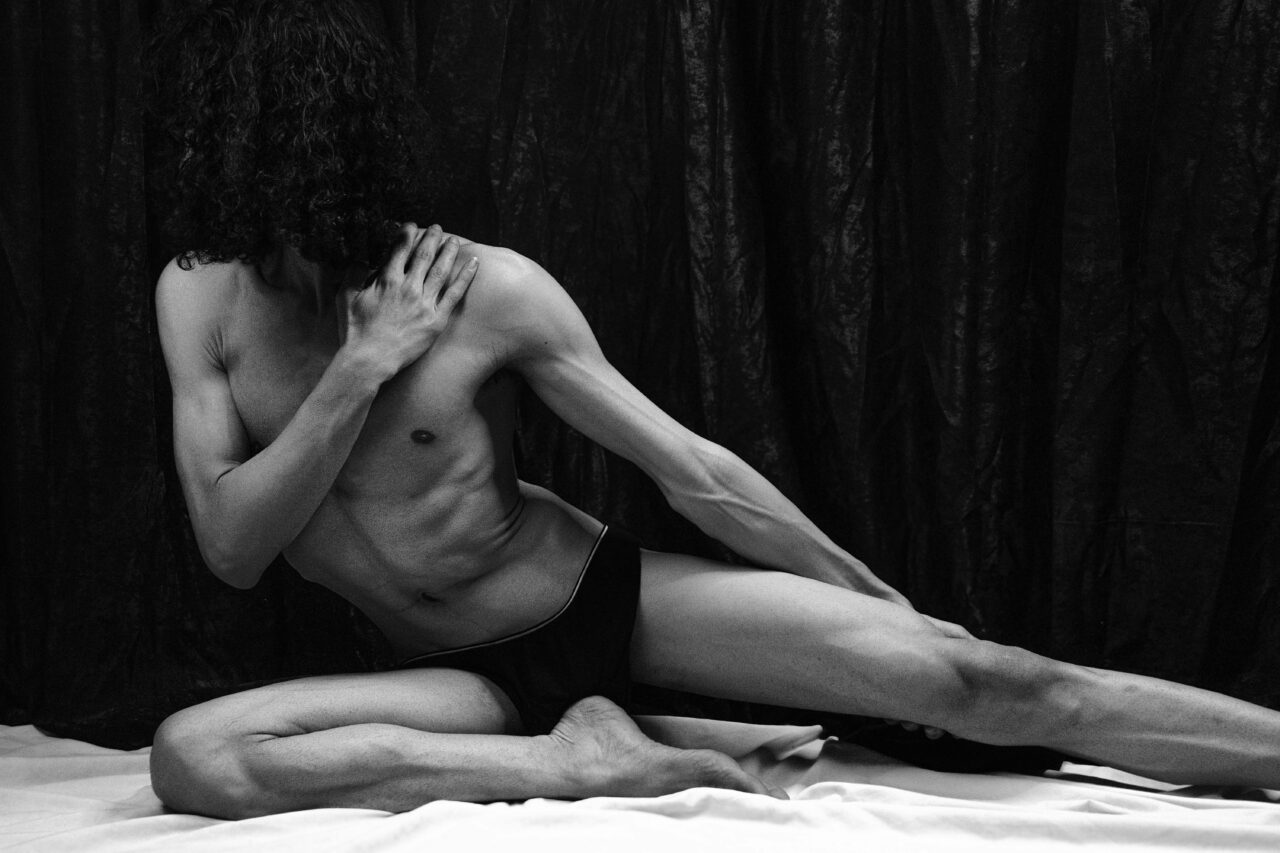 A muscular man stretches in a dramatic black and white portrait, showcasing strength and flexibility.