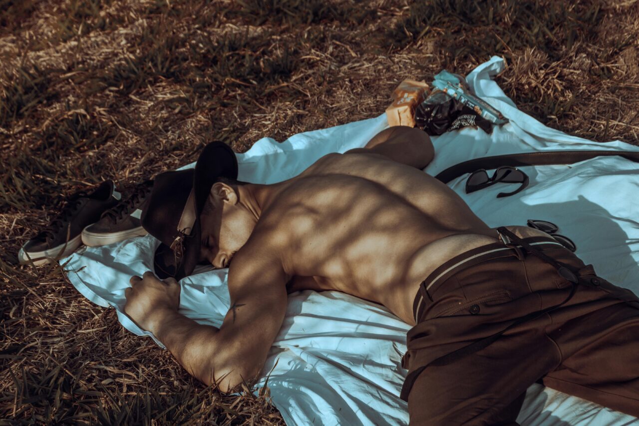 A man in a hat relaxes on a blanket in a sunny meadow, basking in daylight.