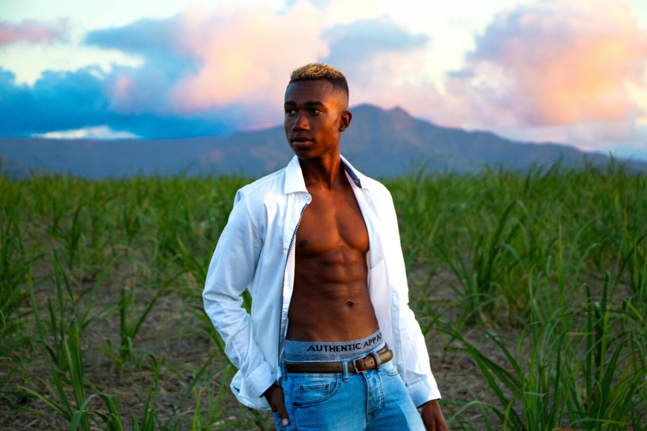 Fashionable young man poses in a lush field during a picturesque sunset in Flic en Flac, Mauritius.