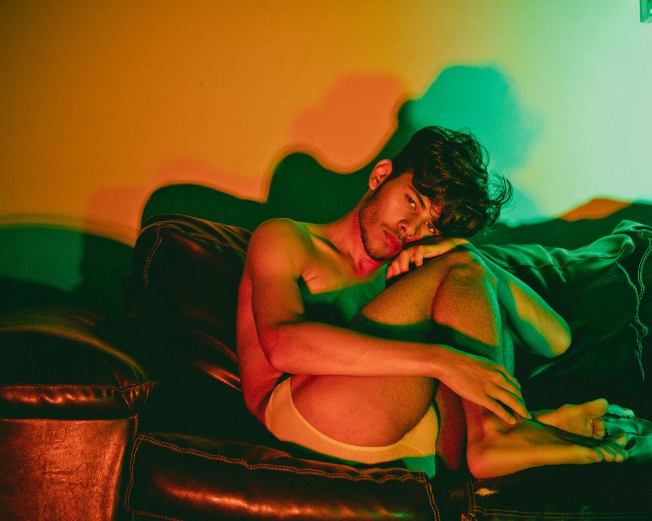 A man sits on a sofa in dramatic lighting, evoking feelings of contemplation and solitude.