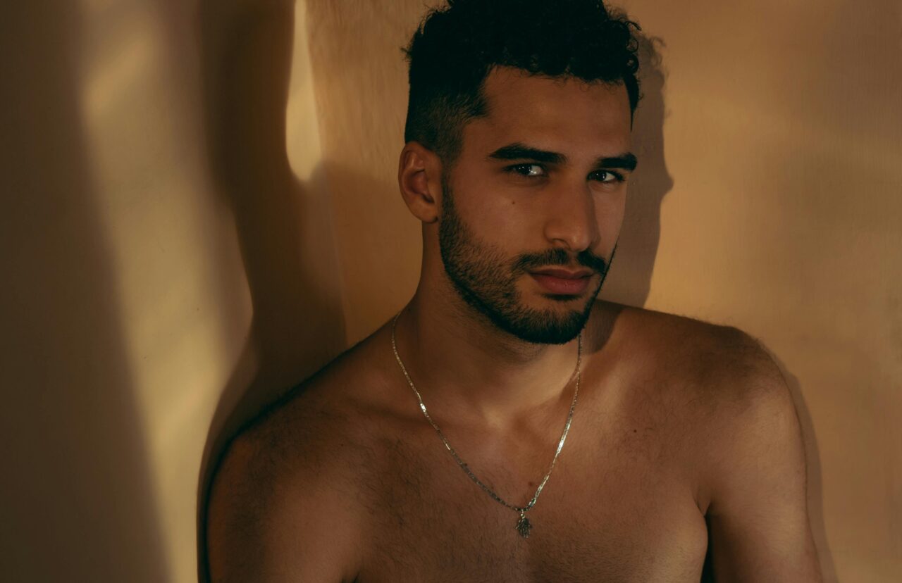 Moody portrait of a shirtless man wearing a necklace, captured indoors.