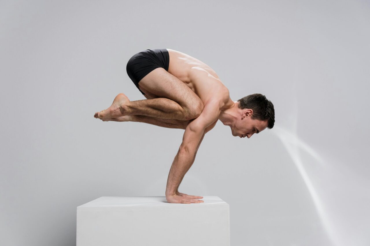 Side view of a man in a yoga arm balance pose indoors, showcasing strength and focus.